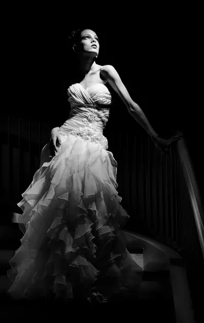 Noiva de vestido longo apoiada no corrimão de uma escada, com luz lateral