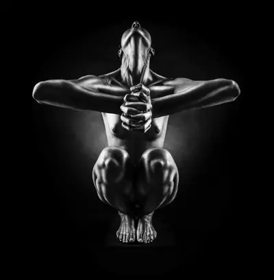 Figura humana agachada, com os braços estendidos à frente, as mãos entrelaçadas e a cabeça inclinada para trás, desenhada pela luz de contorno